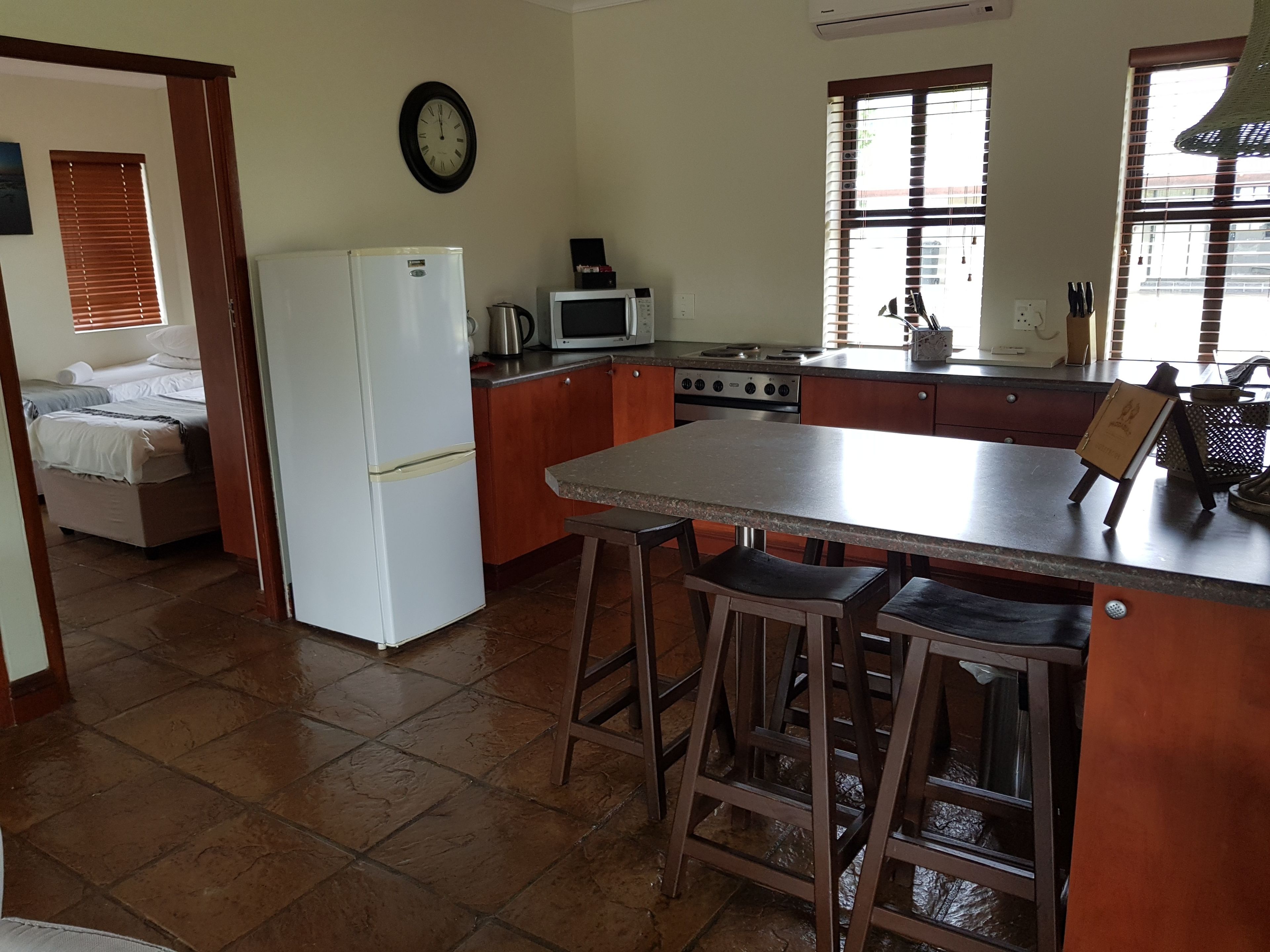 Cozinha compacta com geladeira, micro-ondas, fogão e banquetas de madeira.