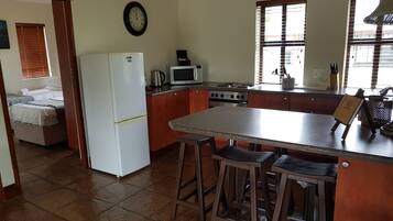 Cozinha compacta com geladeira, micro-ondas, fogão e banquetas de madeira.