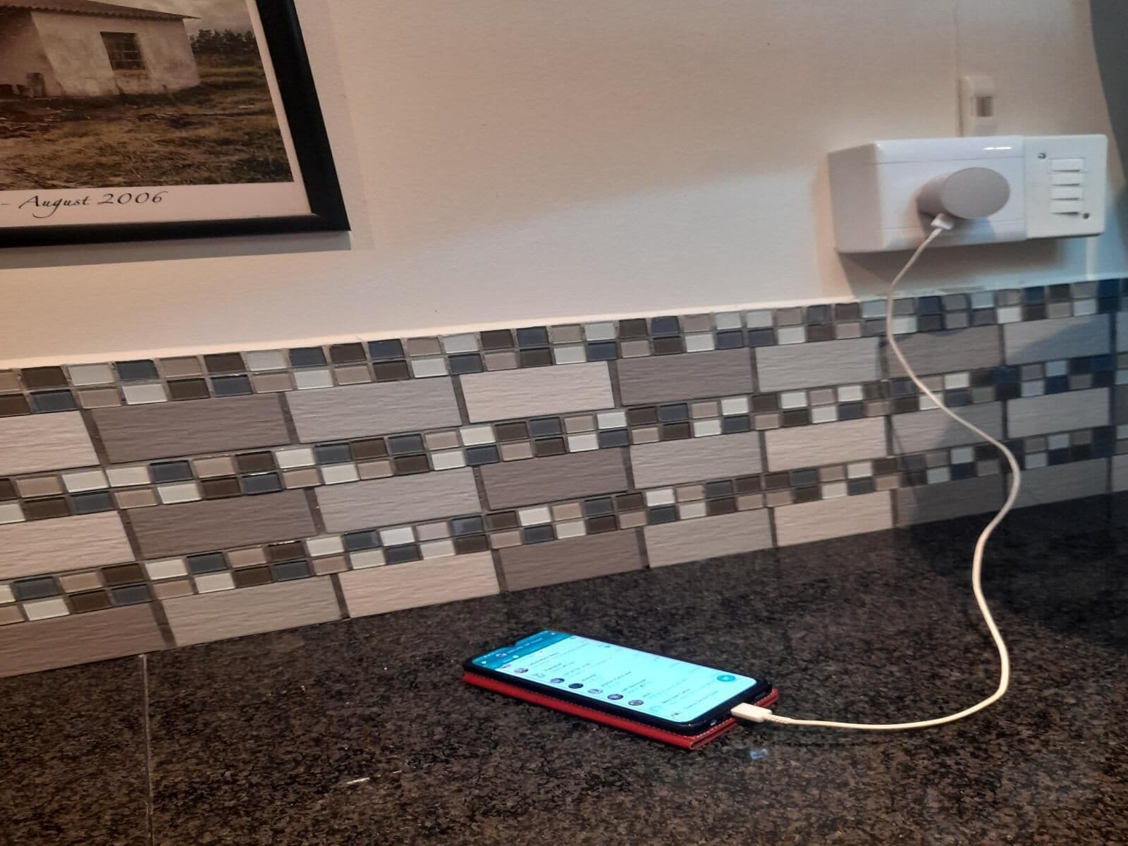 Un teléfono inteligente sobre una encimera de granito, conectado a una toma de corriente en la pared.