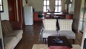 Una sala de estar con un sofá, dos sillones, una mesita de centro y una cocina al fondo.