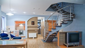 A modern kitchen with a curved staircase, a dining area with blue chairs, and a television on a stand. - First Choice Apartments (Chisinau)