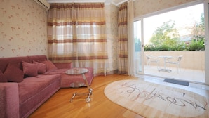A living room with a pink sofa, a glass coffee table, and a round rug with graffiti. There is a sliding glass door leading to an outdoor patio with a table and chairs. - First Choice Apartments (Chisinau)