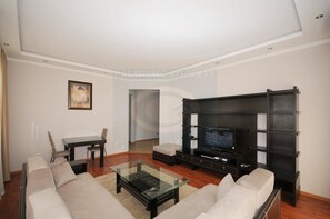 A modern living room with a sofa set, a glass coffee table, a TV on a black entertainment unit, and a painting on the wall. - First Choice Apartments (Chisinau)