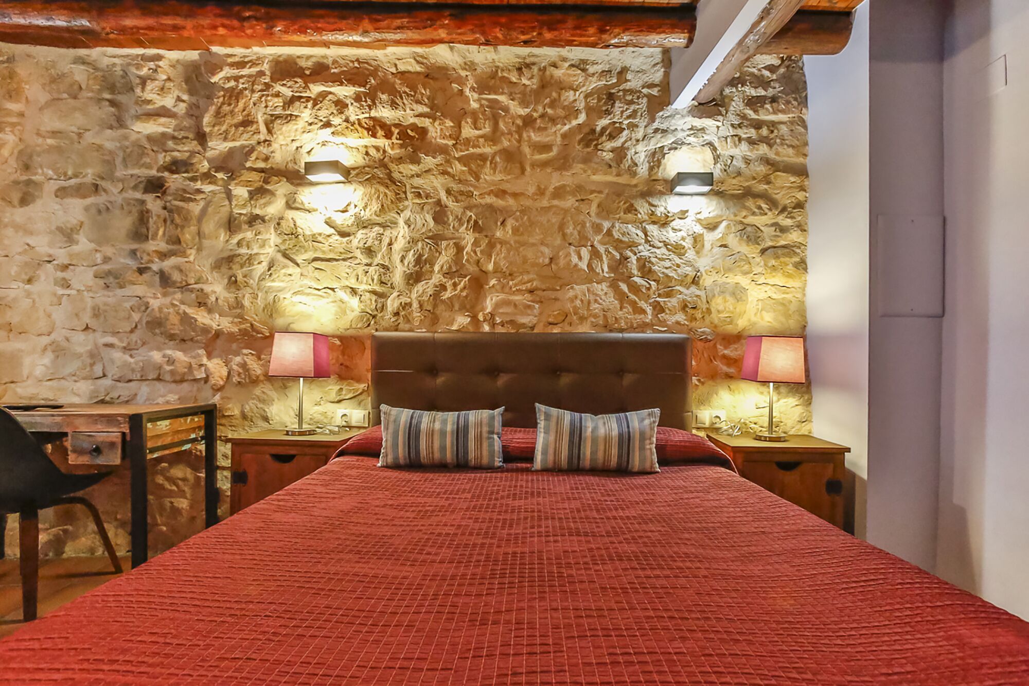 A bedroom with a stone wall, a wooden headboard, and two bedside lamps.