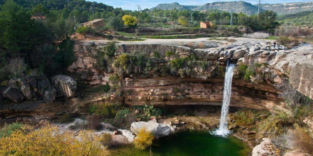 A natural landscape with a waterfall, rocky terrain, and a small pool.