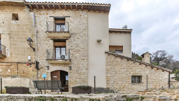 A stone building with a balcony, a wooden door, and a bench outside. - La Grancha (La Fresneda)