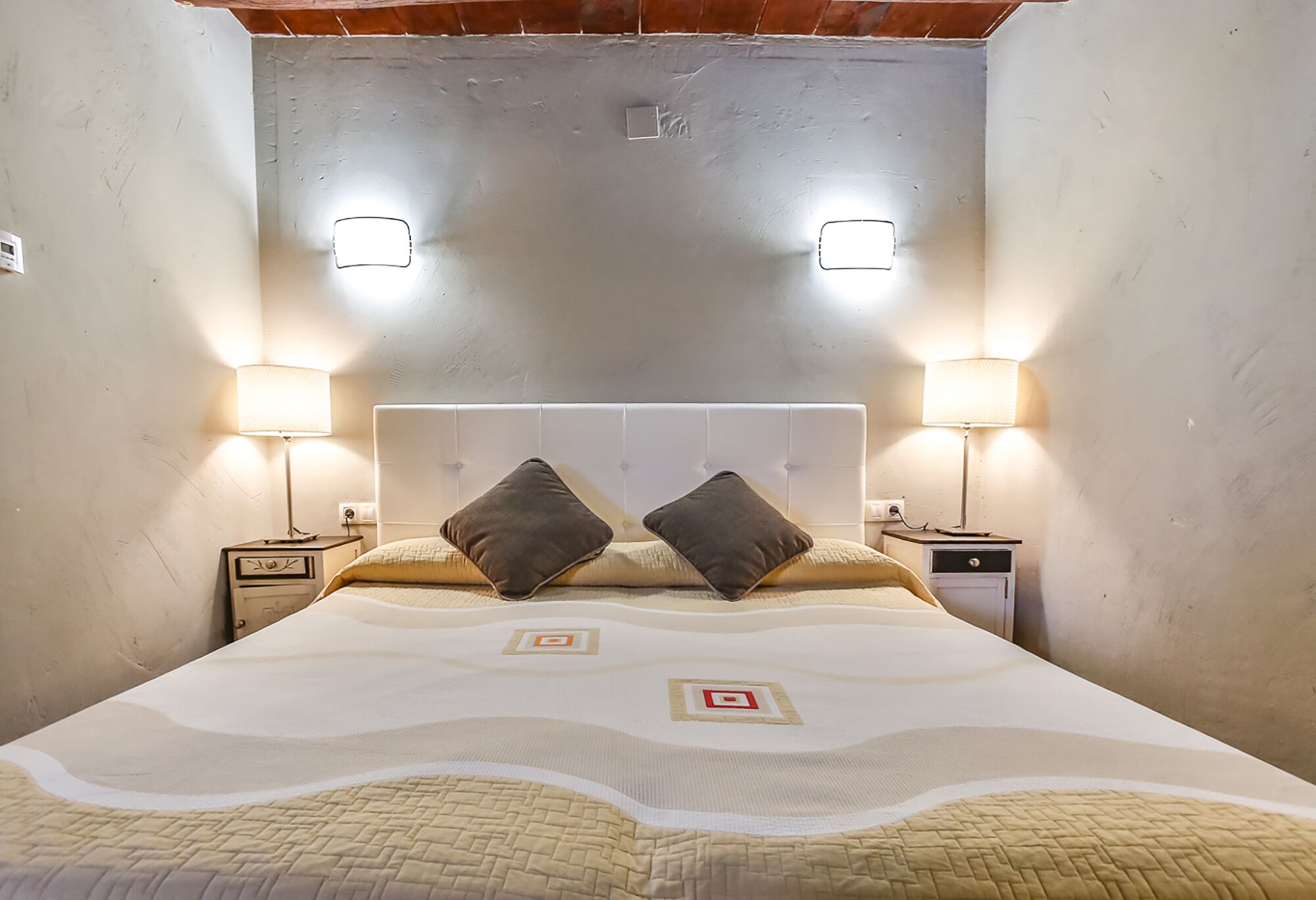 Un dormitorio con una cama grande, dos mesitas de noche, dos lámparas de pared y un cabecero.
