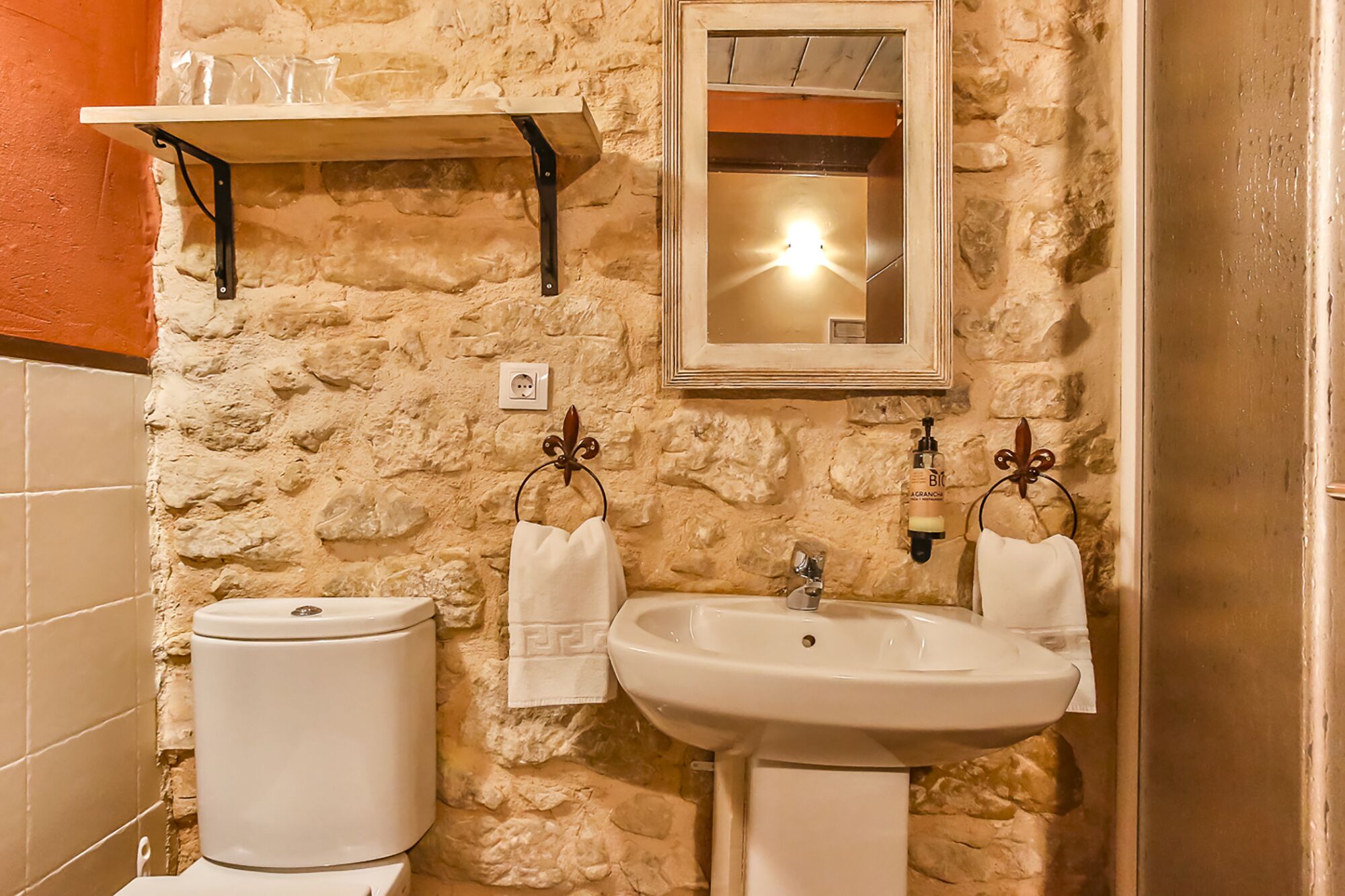 Un bagno con parete in pietra, un lavandino bianco, un water e uno specchio.