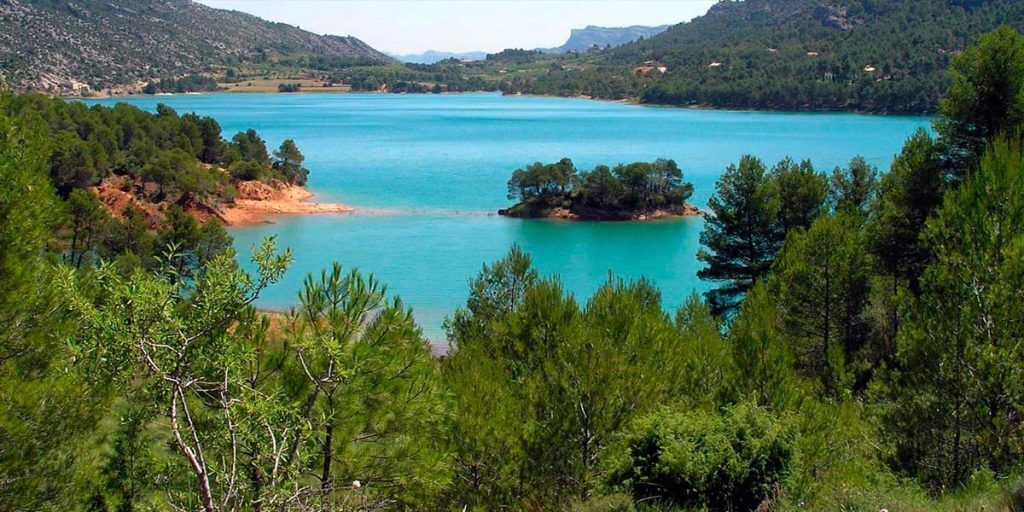 Un paisaje costero con un lago turquesa, rodeado de densos bosques y colinas verdes.