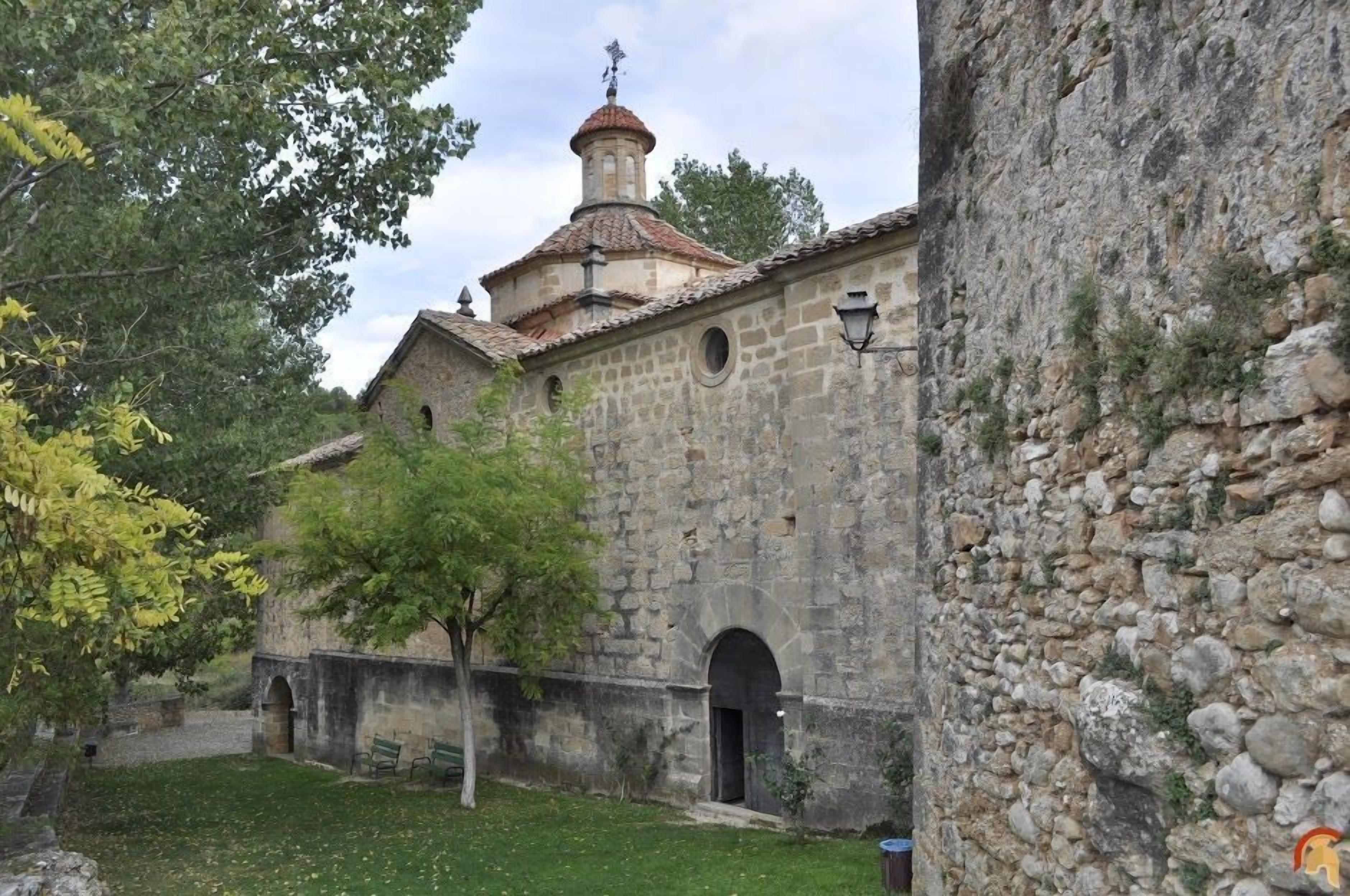 Ein Steinhaus mit einem Glockenturm, Rundbogenportalen und einem kleinen Innenhof mit Bänken.