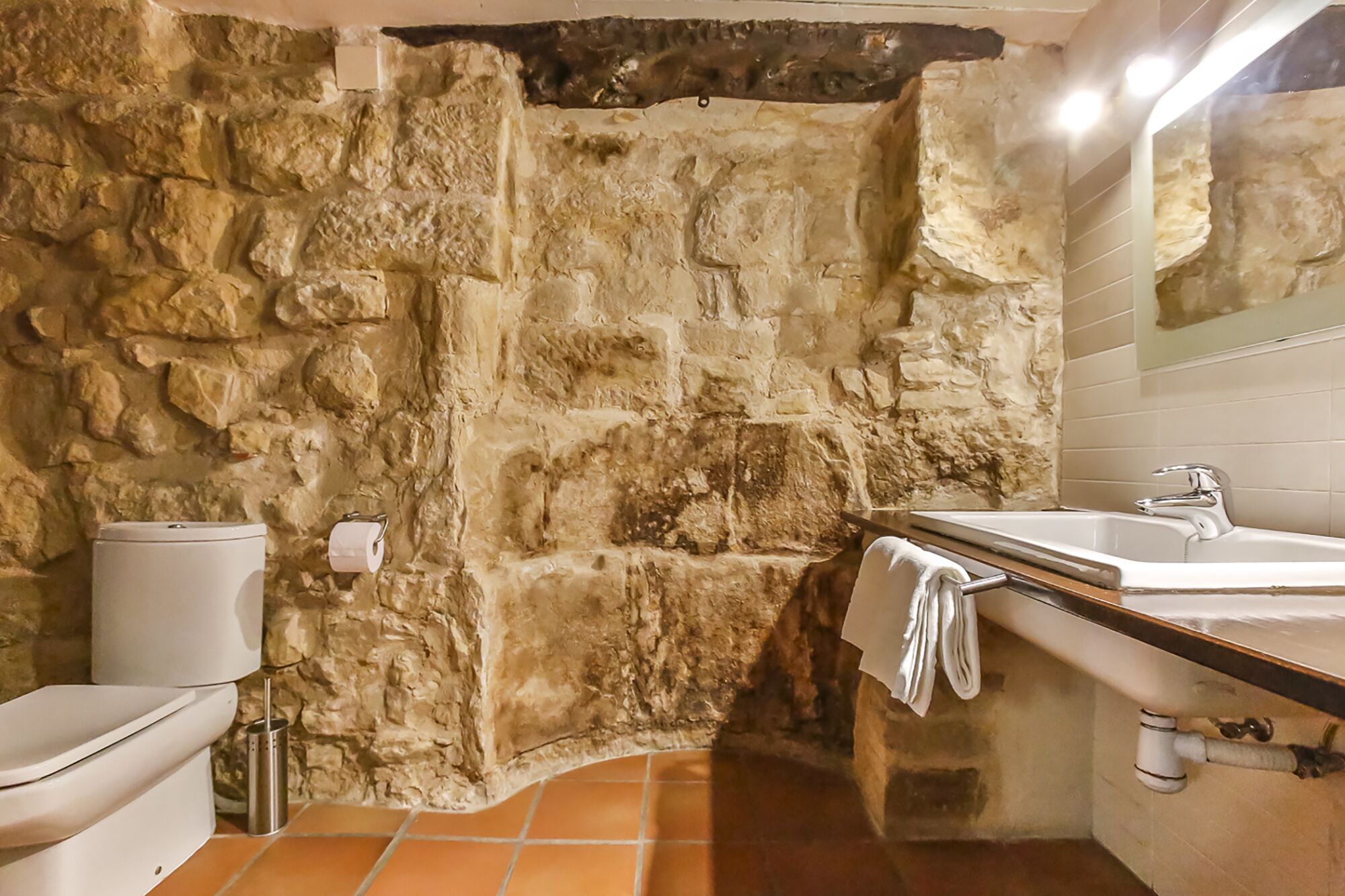 A bathroom with a stone wall, a toilet, a sink, and a mirror.