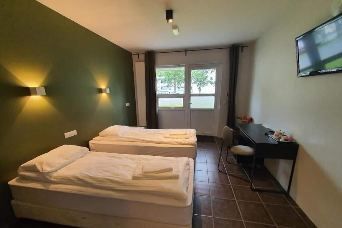 A room with two beds, a desk, a chair, a TV, and a window with curtains.