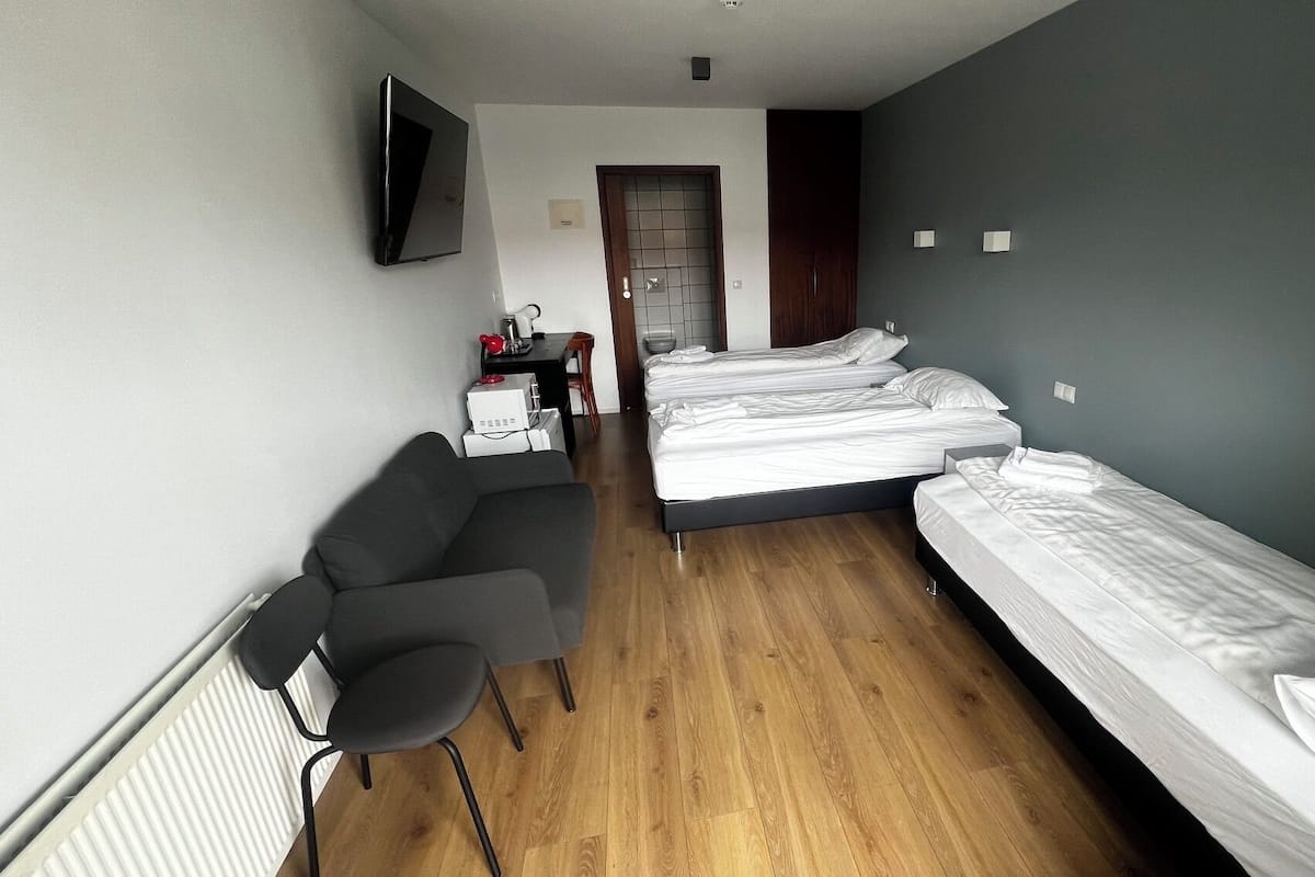 A hotel room with a bed, a desk with a chair, a TV, and a door leading to another room.