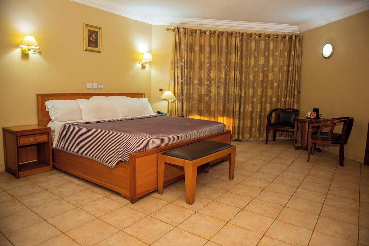 Ein Hotelzimmer mit einem hölzernen Bett, Nachttischlampen, einem Schreibtisch mit Stuhl und einem Vorhang.
