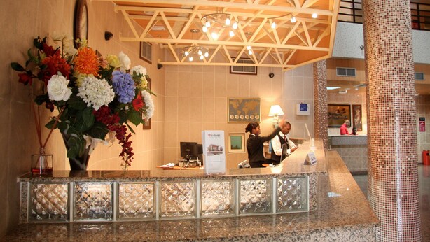 Ein Hotel-Rezeptionsbereich mit einer großen Blumenkomposition, einem Empfangstresen und einer hohen Decke mit freiliegenden Balken und Hängeleuchten.