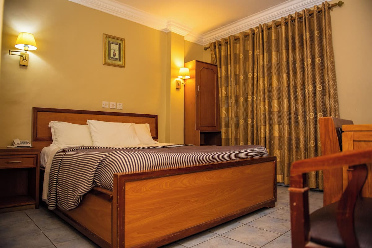 Ein Hotelzimmer mit einem hölzernen Bett, zwei Nachttischlampen, einem Nachttisch, einem Holzschrank und einem Sessel.