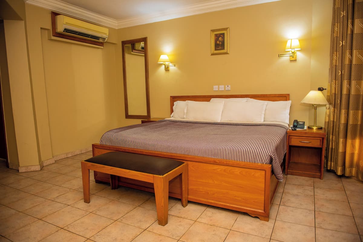 Ein Hotelzimmer mit einem hölzernen Bett, einer Bank, einem Nachttisch, einer Lampe und einer Klimaanlage.