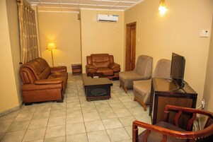 Una sala de estar con un sofá de cuero marrón, un sillón de cuero marrón, un sillón beige, una mesa de centro de madera y un mueble para televisión.