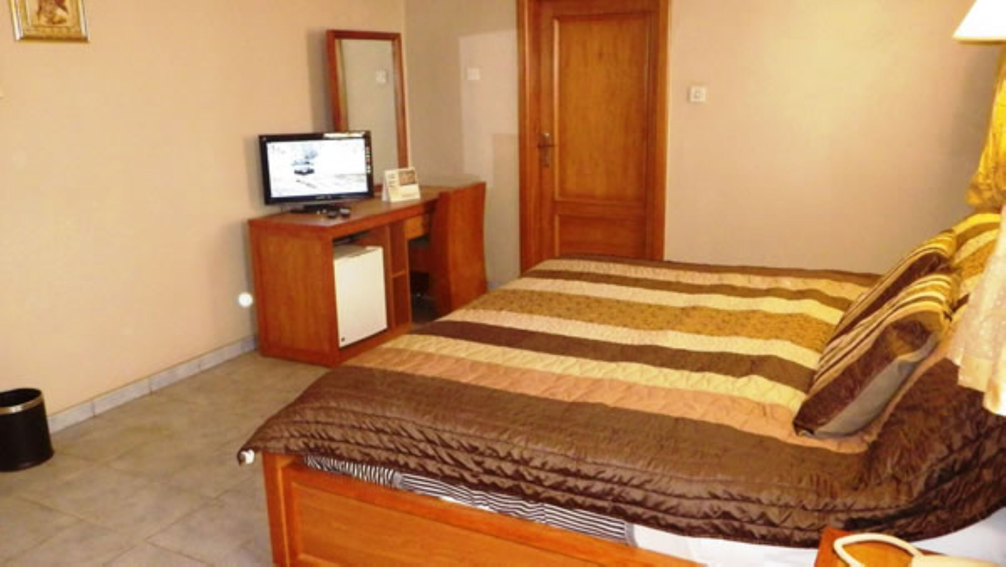 Ein Schlafzimmer mit einem Bett, einer Holzkommode, einem Fernseher und einer Tür.
