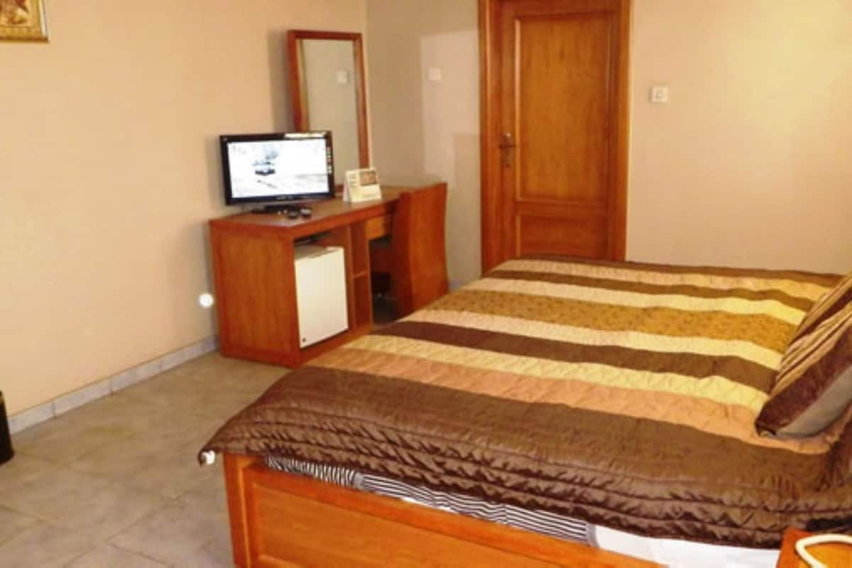 Ein Schlafzimmer mit einem Bett, einer Holzkommode, einem Fernseher und einer Tür.