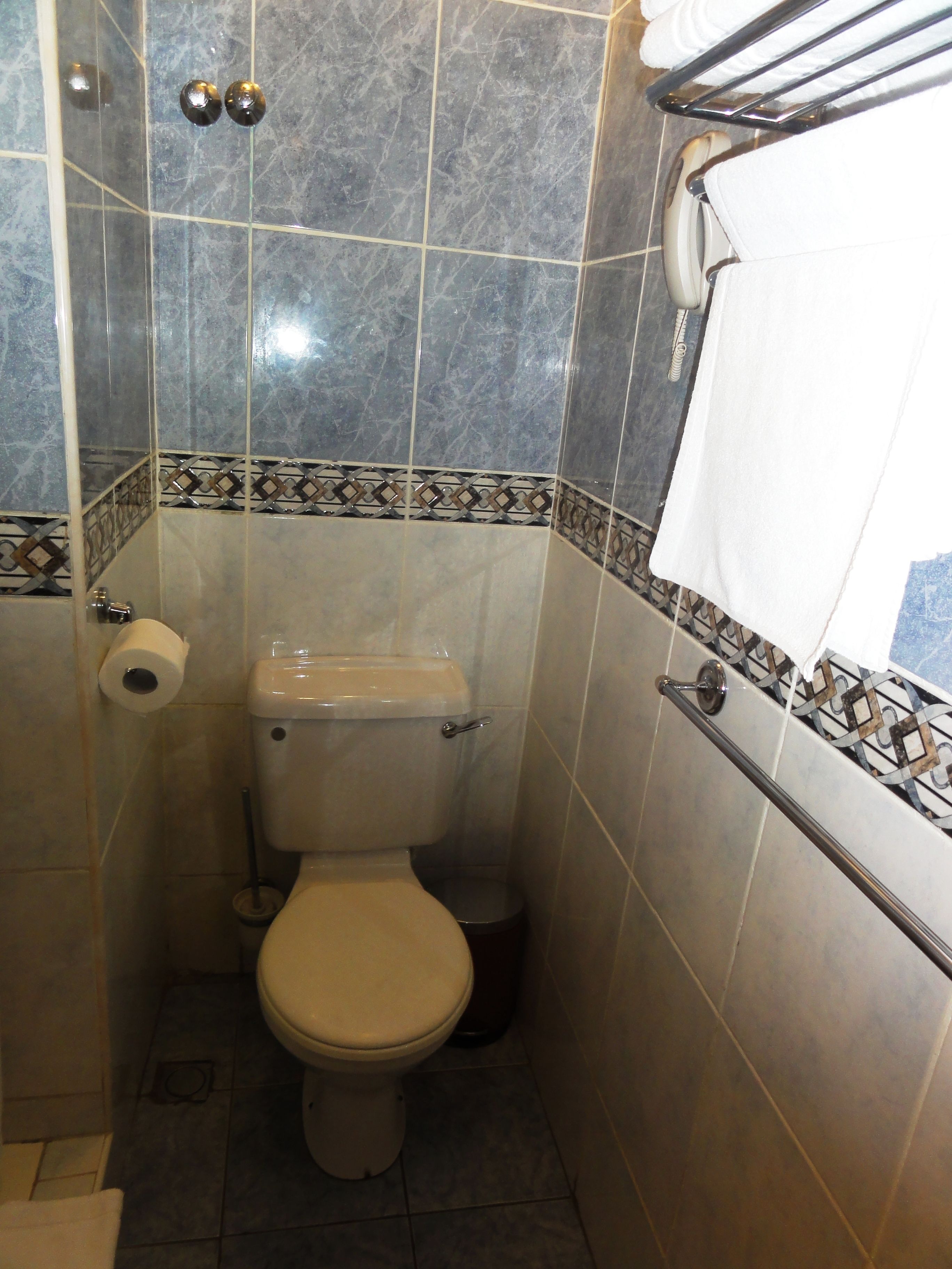 A small, tiled bathroom with a toilet, a hand dryer, and a towel rack.