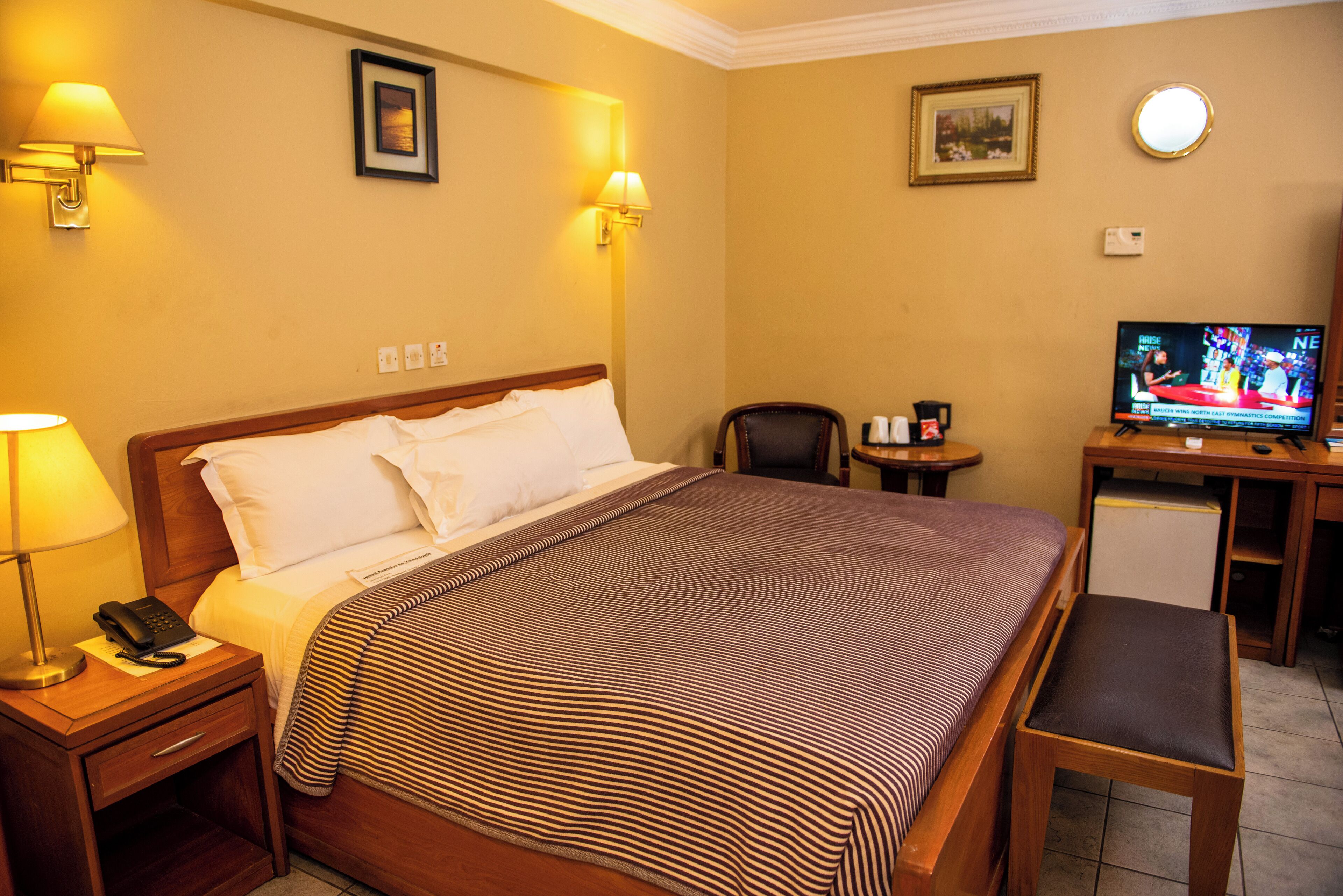 Una habitación de hotel con cama, lámparas de noche, escritorio con televisor y una silla.
