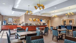 A hotel dining area with multiple tables and chairs, a kitchen area, and decorative lighting.