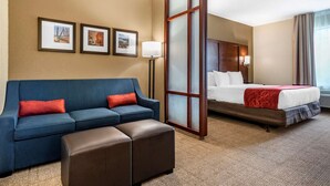 A hotel room with a blue sofa, a bed with a red blanket, a large window, and two framed pictures on the wall.