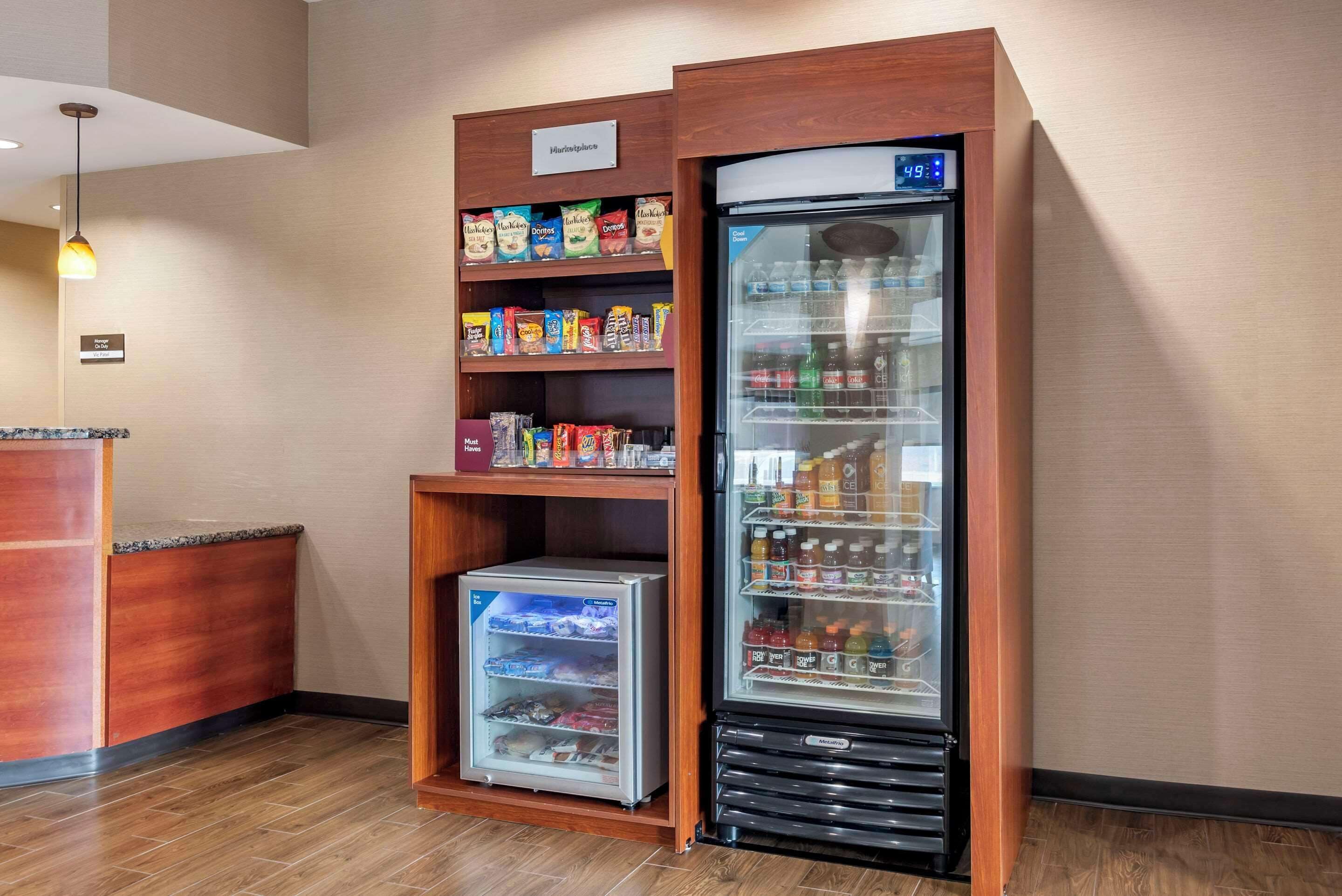 Un dispensador automático de bebidas con pantalla digital, una sección refrigerada y estantes llenos de aperitivos y bebidas.