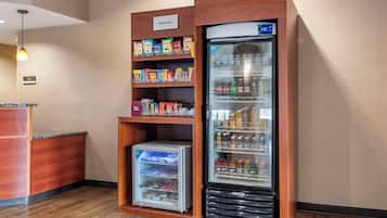 Un dispensador automático de bebidas con pantalla digital, una sección refrigerada y estantes llenos de aperitivos y bebidas.