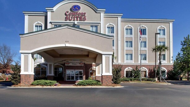 A Comfort Suites hotel with a prominent entrance, a brick facade, and a clear blue sky.