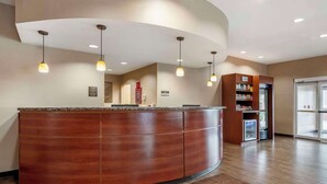 A reception area with a curved wooden counter, pendant lighting, a refrigerator with snacks, and a glass door leading outside.