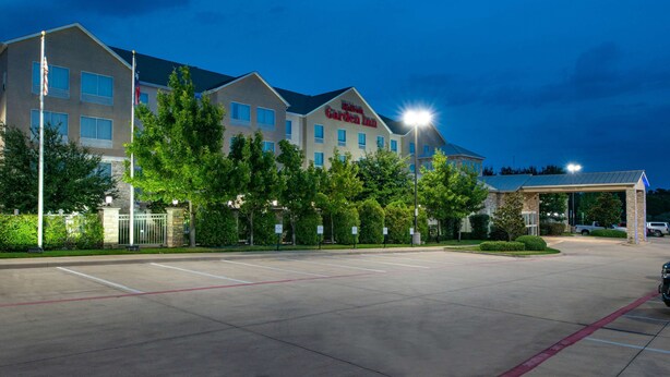 A hotel with a large parking lot, a covered entrance, and a well-lit facade. - Hilton Garden Inn Denton (Denton)
