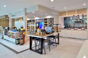 A modern cafe with a self-service coffee station, seating area, and a visible kitchen. - Hilton Garden Inn Denton (Denton)
