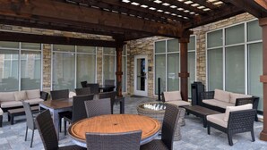 An outdoor patio area with wicker furniture, a round wooden table, and stone walls. - Hilton Garden Inn Denton (Denton)
