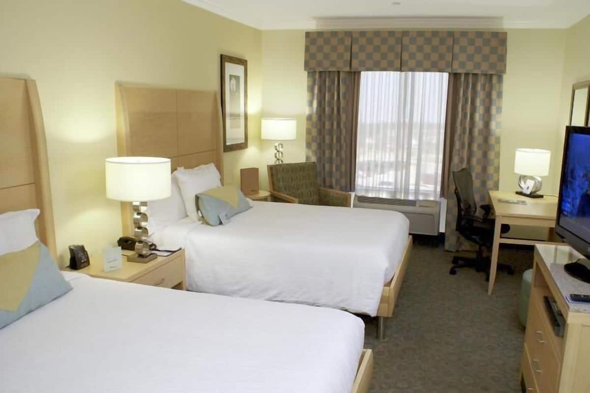 A hotel room with two beds, a desk, a chair, a television, and a window with curtains.