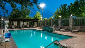 A swimming pool with lounge chairs and a covered seating area, surrounded by stone walls and a fence. - Hilton Garden Inn Denton (Denton)