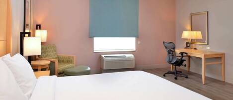 Habitación de hotel con una cama grande, un escritorio, una silla, una mesita, una lámpara, un calentador y una ventana con persiana.