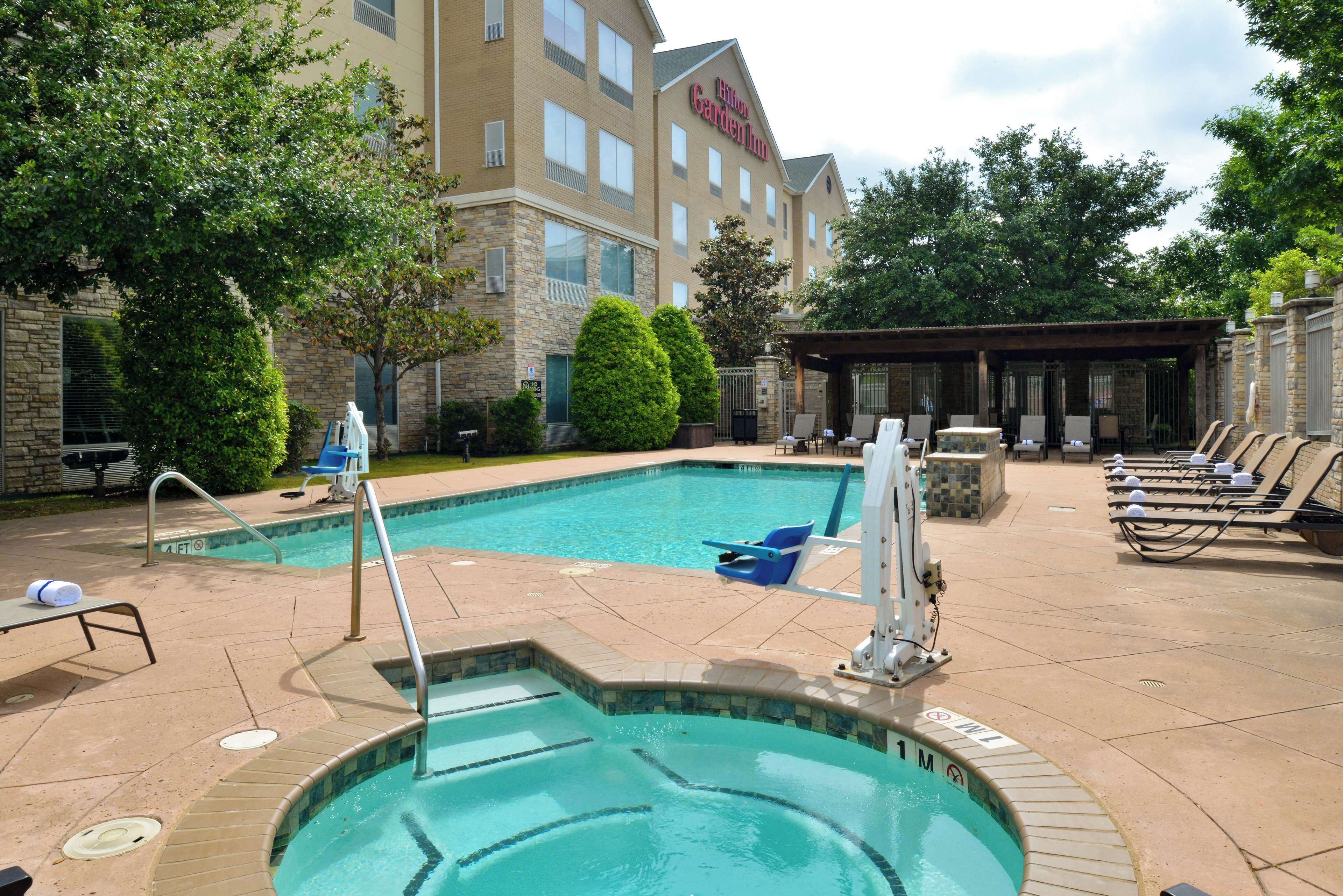 A hotel pool area with a hot tub, lounge chairs, and a covered seating area.