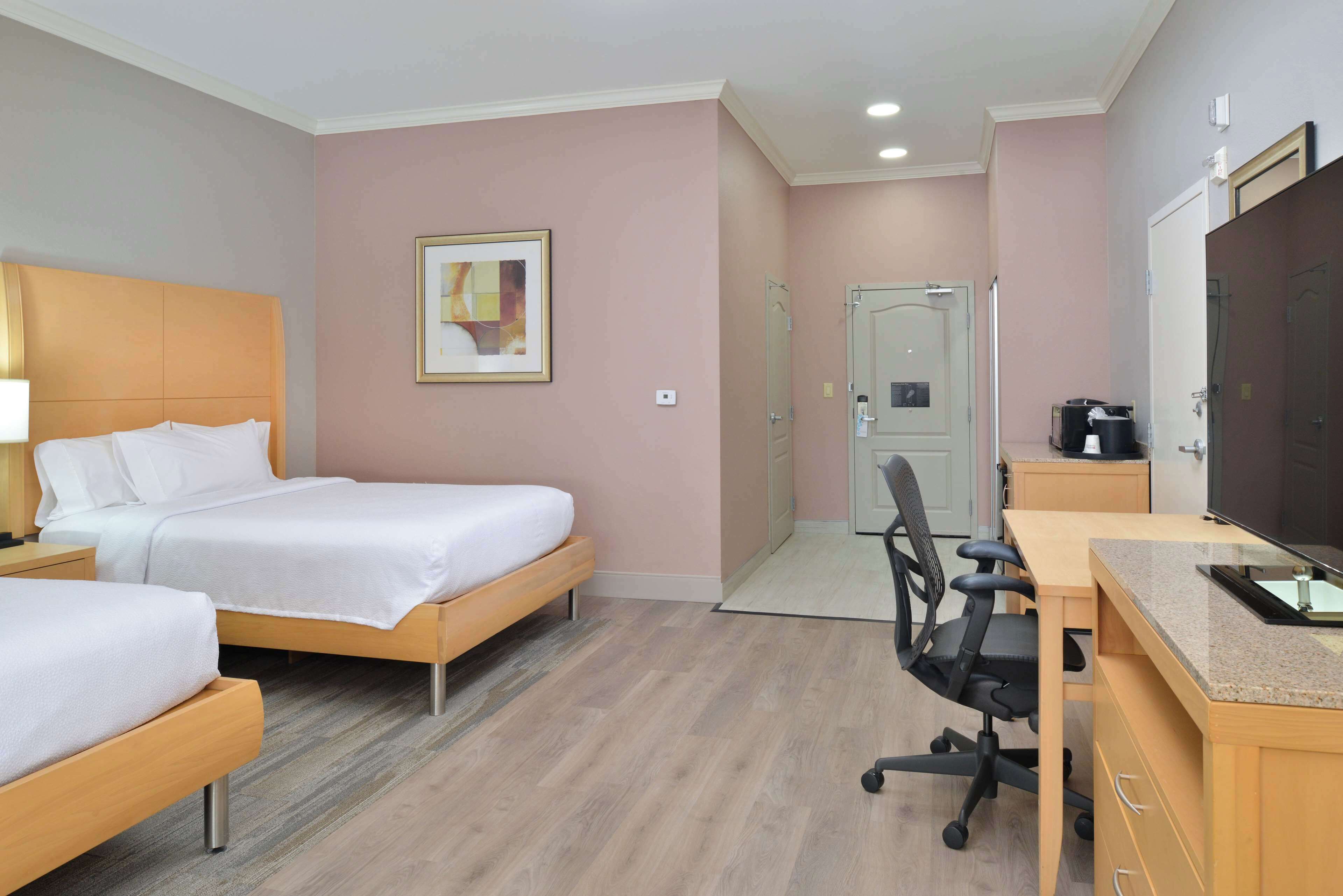 Ein Hotelzimmer mit zwei Betten, einem Schreibtisch, einem Stuhl, einem Fernseher und einer Badezimmertür.
