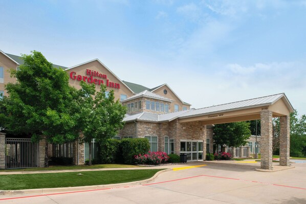 A hotel with a stone facade, a covered entrance, and a clear sky. - Hilton Garden Inn Denton (Denton)