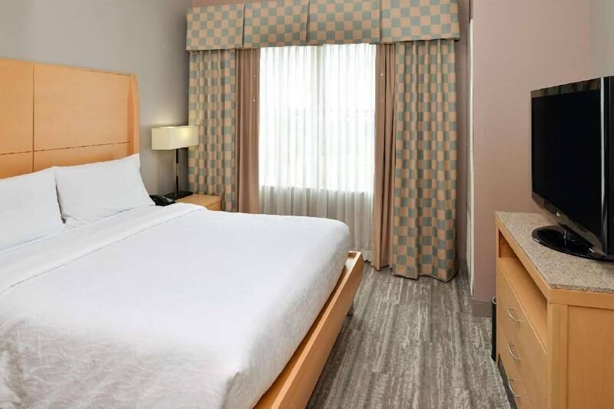 A hotel room with a bed, a television, a nightstand, and a window with curtains.