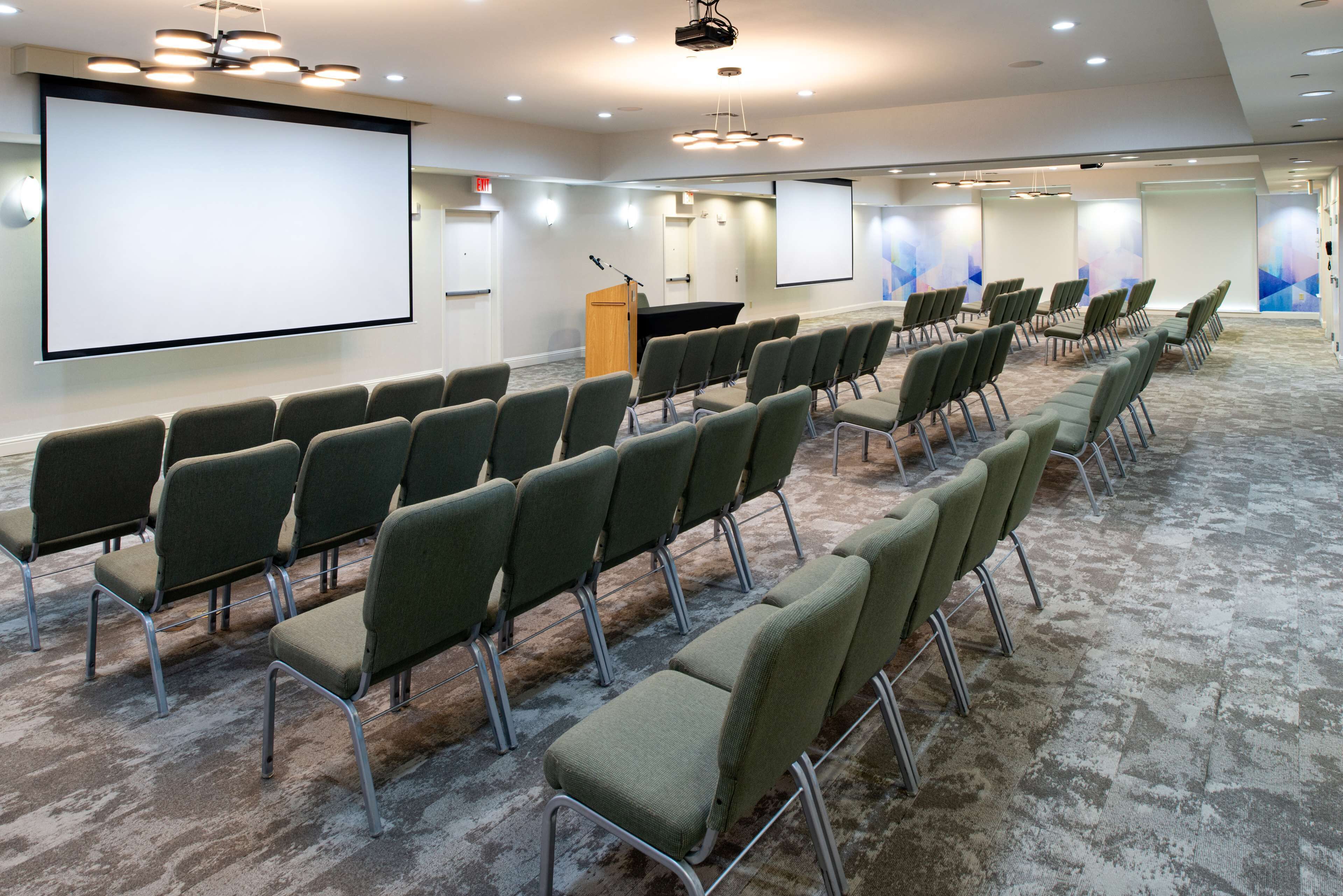 A conference room with rows of chairs, a podium, and a large screen.