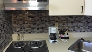 A kitchen with a gas stove, a coffee maker, a sink, and a tiled backsplash. - East Street Inn & Suites Tipton (Tipton)