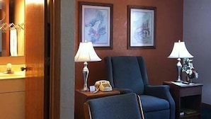 A hotel room with a wooden door, a blue armchair, a small table with a lamp, and two framed pictures on the wall. - East Street Inn & Suites Tipton (Tipton)