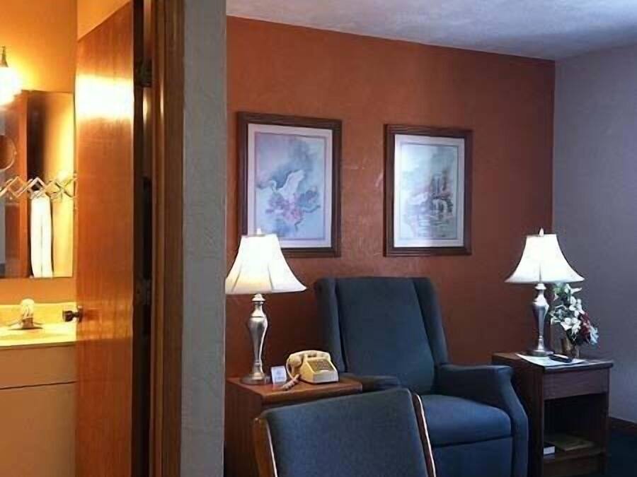 A hotel room with a wooden door, a blue armchair, a small table with a lamp, and two framed pictures on the wall.