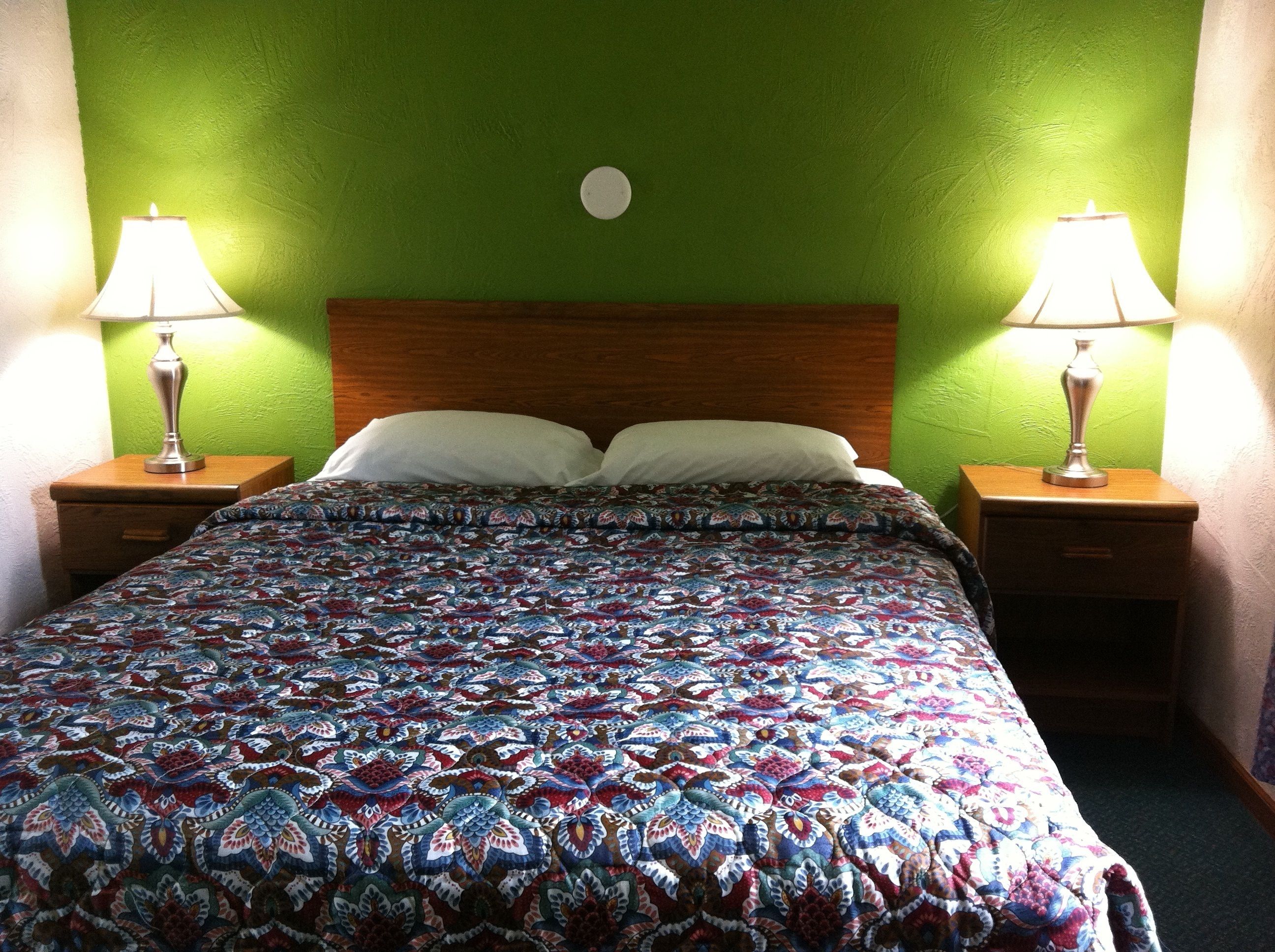 A bed with a patterned bedspread, two bedside lamps, and a green wall.