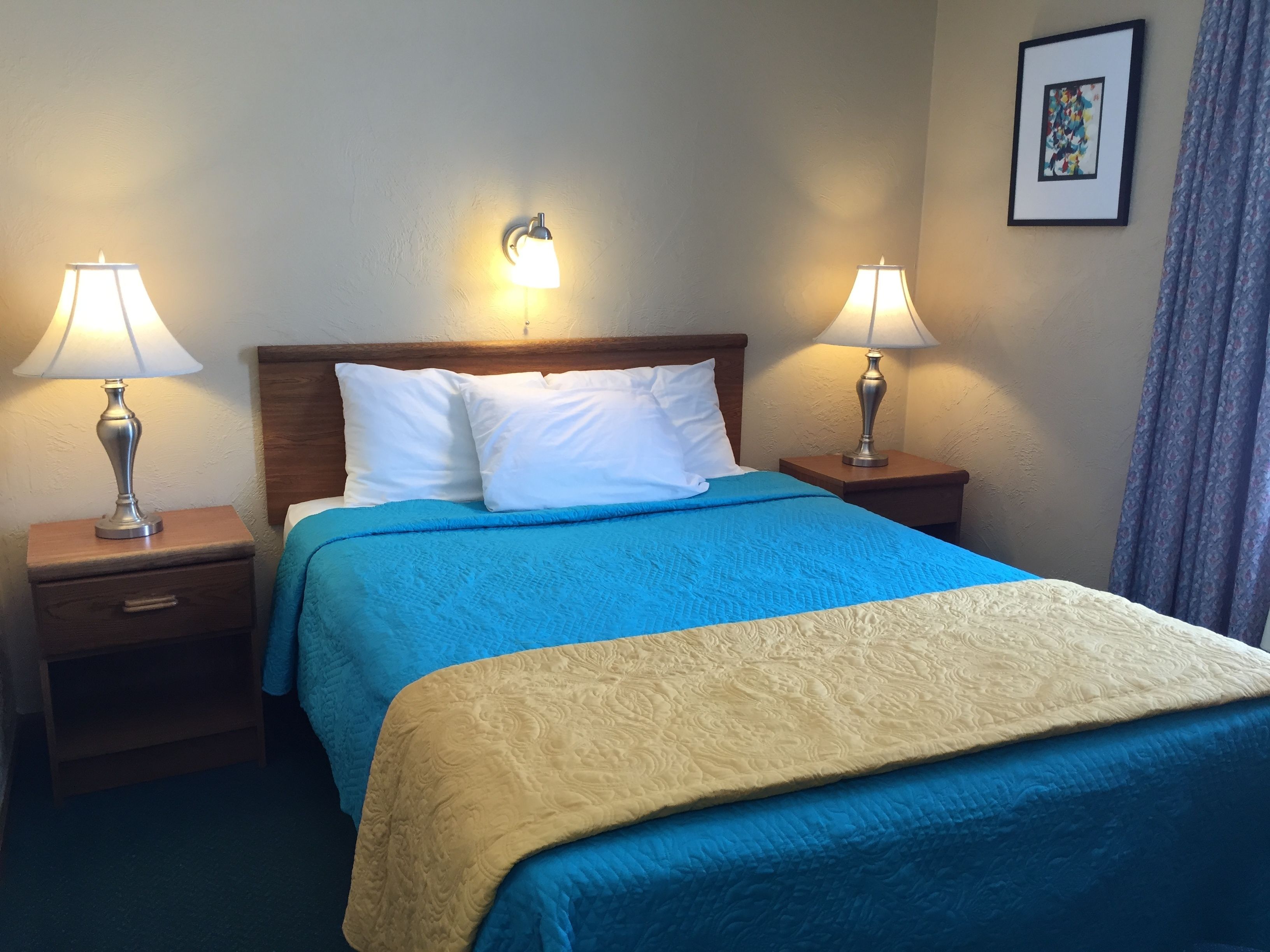 Ein Hotelzimmer mit einem Bett, zwei Nachttischlampen, einem Nachttisch und einem gerahmten Bild an der Wand.
