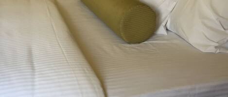 A neatly made bed with white linens and a single green pillow.