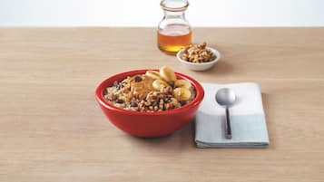 A bowl of cereal with a spoon and a bottle of syrup on a wooden table.